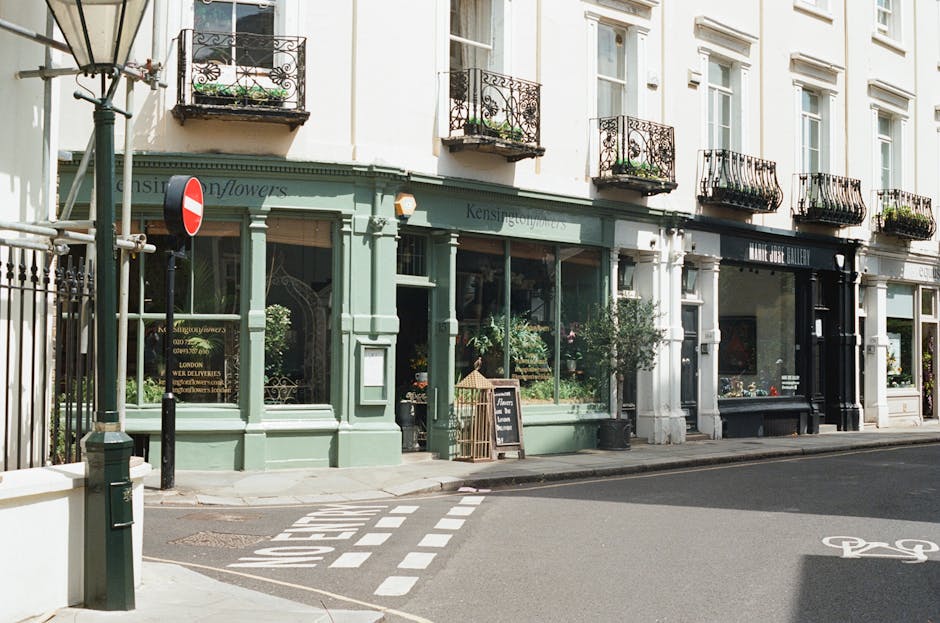 A wide outdoor view of the Royal Albert Hall in South Kensington, London, showing its distinctive circular brick and stone façade with arched windows and a large dome roof. In the foreground, a paved