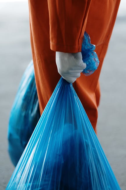 Two men engaged in waste disposal outside a property during a home relocation process, with one man wearing a black jacket and yellow gloves lifting a cardboard box filled with waste and debris while 